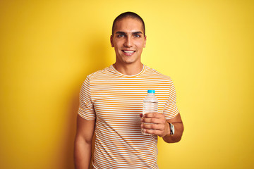 Young handsome man holding plastic water bottle over yellow isolated background with a happy face standing and smiling with a confident smile showing teeth