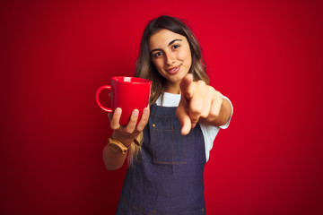 Sticker - Young beautiful barista woman wearing apron over red isolated background pointing with finger to the camera and to you, hand sign, positive and confident gesture from the front