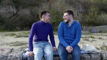 Two Gay Guys From The LGBT Community Are Sitting On A Stone Pier In A Sweater And Sweatshirt, Blue And Laughing, After Which One Puts His Head On The Shoulder Of The Other