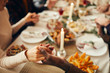 © Seventyfour - Closeup of people sitting at dining table on Christmas and joining hands in prayer, copy space