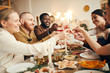 © Seventyfour - Multi-ethnic group of people raising glasses sitting at beautiful dinner table celebrating Christmas with friends and family, copy space