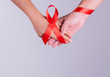 World AIDS Day. Holding hands with Red ribbon over grey background.