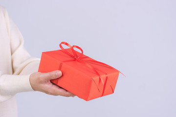 Closeup hands giving gift box. Woman deliveries a red package gift with red ribbon. Holiday/ birthday/ Christmas concept banner.