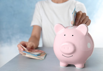 Wall Mural - Woman putting Euro banknote into piggy bank at table indoors, closeup. Money savings