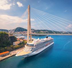 Aerial view of cruise ship and beautiful bridge in Dubrovnik, Croatia. Top view of large ship and road at sunset. Summer landscape with harbor, mountain, blue sea and green trees. Cruise liner in port