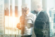 © Mongkolchon - business background of two businessman standing together with hands holding a cup of coffee during having business talking, view through office window