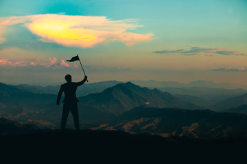 Silhouette of a man standing with a victory flag on the top of the mountain on sunrise sky background,business, success, leadership and achievement concept