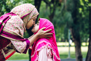 Wall Mural - Portrait of happy lovely family arabic muslim mother and little muslim girls child with hijab dress smiling and having fun hugging and kissing together in summer park