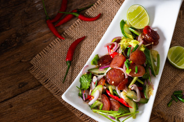 Wall Mural - Spicy Chinese pork sausage with vegetable Thai salad in white plate on wood background