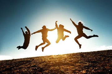 Four jumping silhouettes friends against sun