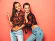 © halayalex - Two young beautiful smiling brunette hipster girls in trendy similar checkered shirt and jeans clothes.Sexy carefree women posing near pink wall in studio.Positive models having fun