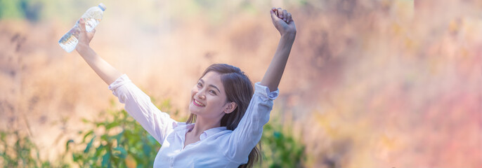 Woman holding a bottle of drinking water and raised arms in the nature.