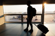 © twinsterphoto - Young male solo travel backpacker walks and drags bag trolley in the airport against sunlight with airplanes in background - adventure holiday and air plane transportation concept