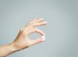 Female hand holding a round white pill or vitamin.