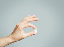 Female Hand Holding A Round White Pill Or Vitamin.