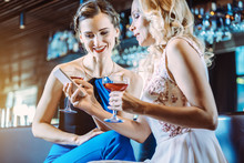 Two Women In A Bar Looking At Their Mobile Phone