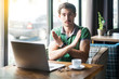 This is the end. Young serious businessman in green t-shirt sitting and looking at camera showing closed or x sign with hands. business and freelancing concept. indoor shot near big window at daytime.