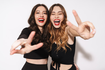 Wall Mural - Portrait of two excited women laughing and gesturing peace sign