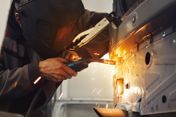 Worker repairing car body with carbon dioxide welding. Weld of auto.