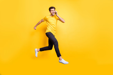 Poster - I'm on my way darling. Full body photo of handsome guy jumping high talking telephone rushing romantic date wear casual t-shirt trousers isolated yellow color background