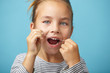 Caucasian child girl using a dental floss on blue isolated background and smiling while looking to the camera.