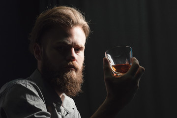 Portrait of a pensive handsome young man, with a glass of alcohol in his hands.