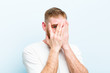 © kues1 - young red head man covering face with hands, peeking between fingers with surprised expression and looking to the side against soft blue background