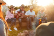© Monkey Business - Group Of Mature Friends Sitting Around Fire As They Drink And Sing Songs At Outdoor Campsite