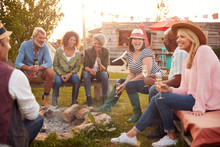 Group Of Mature Friends Sitting Around Fire And Drinking At Outdoor Campsite Bar
