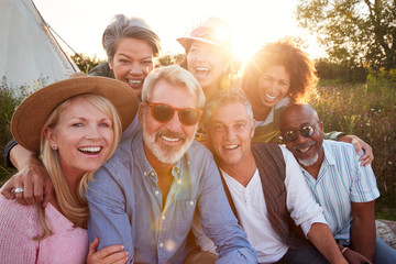 portrait of mature friends by tent on camping vacation against setting sun