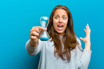 Wall Mural - young woman with sand timer  against blue background