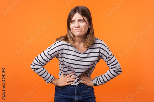 Cuadros en Lienzo Portrait of unhappy ill woman with brown hair in long sleeve striped shirt standing, holding her belly with hands, stomach cramps or period pain