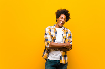Wall Mural - young black man looking like a happy, proud and satisfied achiever smiling with arms crossed against orange wall