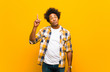 © kues1 - young black man feeling like a genius holding finger proudly up in the air after realizing a great idea, saying eureka against orange wall