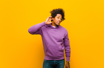 Wall Mural - young black man looking serious and curious, listening, trying to hear a secret conversation or gossip, eavesdropping against orange wall
