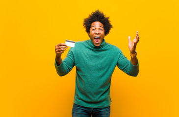 Wall Mural - young african american man with a credit card against orange bac