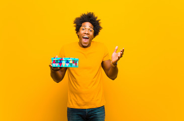 Wall Mural - young african american man with a gift box against orange backgr