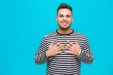 Wall Mural - young hispanic man looking happy, surprised, proud and excited, pointing to self against blue background