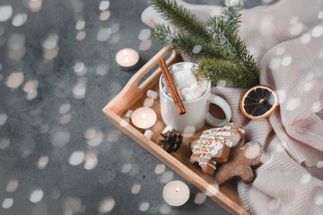 cocoa, hot chocolate with cinnamon and marshmallows, cookies, gingerbread man, spruce branch, candles, cone, a slice of dried orange, lights on a gray background, copy space;