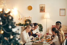 Wide Angle View At Modern Young People Celebrating Christmas Sitting At Dinner Table In Elegant Dining Room, Copy Space