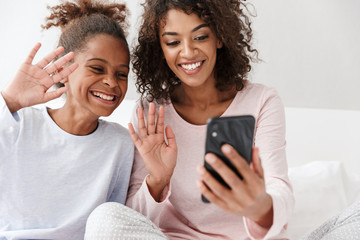 Wall Mural - Image of american woman and her little daughter using cellphone at home