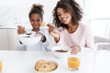 Wall Mural - Image of american woman and her daughter having breakfast in kitchen