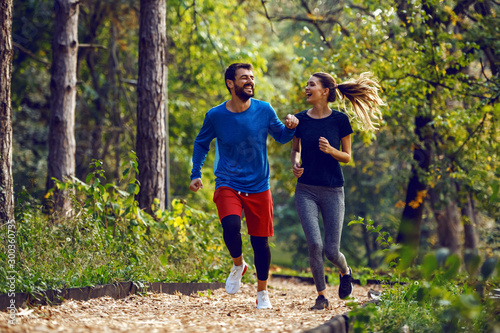 Fotomural Full length of fit sporty happy caucasian couple in sportswear running in woods on trail in morning