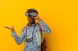 Young african tourist man standing against a yellow background holding a binoculars