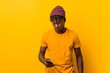© Asier - Young african man standing against a yellow background wearing a hat and using a phone