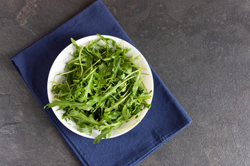 Wall Mural - Fresh green arugula in a white ceramic bowl on black table.