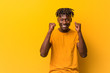 © Asier - Young black man wearing rastas over yellow background raising fist, feeling happy and successful. Victory concept.