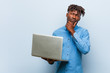 © Asier - Young rasta black man holding a laptop looking sideways with doubtful and skeptical expression.