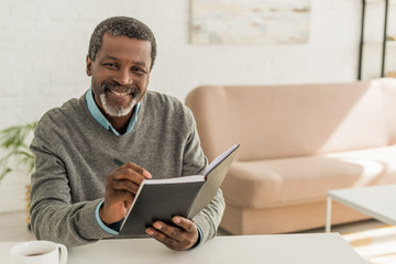 cheerful african american man smiling at camera while holding notebook