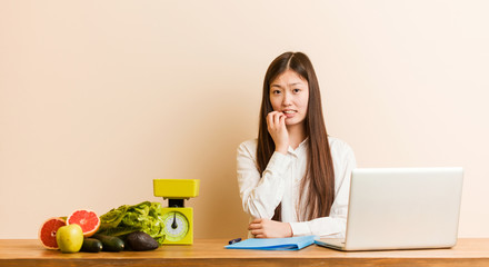 Wall Mural - Young nutritionist chinese woman working with her laptop biting fingernails, nervous and very anxious.